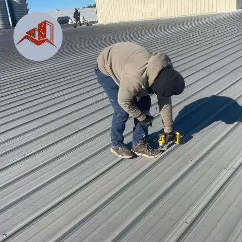 Roofer fastening ribbed gray metal roofing panels on a commercial low-slope roof